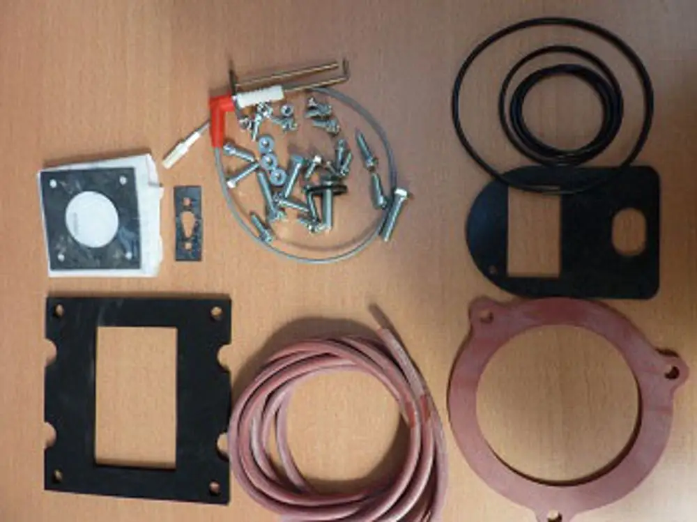 Wartungssatz bestehend aus verschiedenen Dichtungen, Schrauben und einer Z-Elektrode, geeignet für Remeha Produkte, auf einem Holztisch angeordnet.